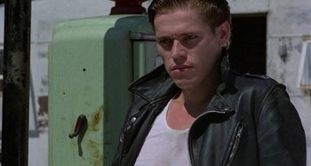 Movie still from “The Loveless” (1981), directed by Kathryn Bigelow – A man in a leather jacket standing in front of an old gas pump; Close Up shot, Low angle