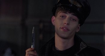 Movie still from “The Loveless” (1981), directed by Kathryn Bigelow – A man in a police uniform holding a knife; Close Up shot, Over the shoulder angle