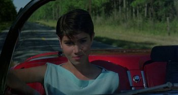 Movie still from “The Loveless” (1981), directed by Kathryn Bigelow – A woman sitting in the driver's seat of a red car; Close Up shot, Low angle