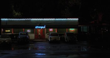 Movie still from “The Loveless” (1981), directed by Kathryn Bigelow – An empty parking lot at night in front of a restaurant; Extreme Wide shot, High angle