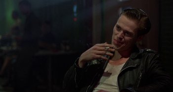 Movie still from “The Loveless” (1981), directed by Kathryn Bigelow – A man sitting down talking on a cell phone; Close Up shot, Low angle