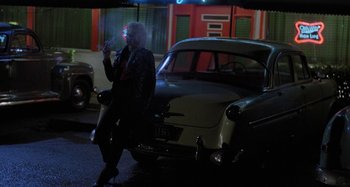Movie still from “The Loveless” (1981), directed by Kathryn Bigelow – A woman standing next to an old car at night; Wide shot, Over the shoulder angle