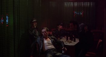 Movie still from “The Loveless” (1981), directed by Kathryn Bigelow – A group of men sitting at a table in a room; Wide shot, High angle