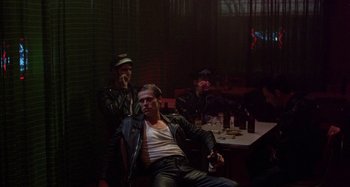Movie still from “The Loveless” (1981), directed by Kathryn Bigelow – A group of men sitting at a table in a room; Wide shot, Over the shoulder angle