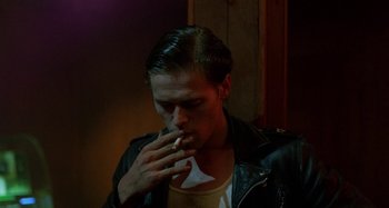 Movie still from “The Loveless” (1981), directed by Kathryn Bigelow – A man in a leather jacket is eating a piece of paper; Close Up shot, Over the shoulder angle