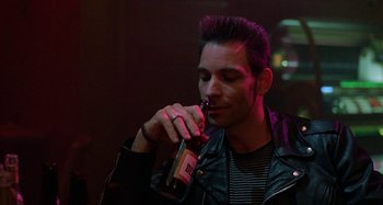 Movie still from “The Loveless” (1981), directed by Kathryn Bigelow – A man holding a bottle of beer in his hand; Close Up shot, Over the shoulder angle