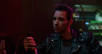 Movie still from “The Loveless” (1981), directed by Kathryn Bigelow – A man in a leather jacket holding a cell phone; Close Up shot, Over the shoulder angle