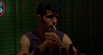 Movie still from “The Loveless” (1981), directed by Kathryn Bigelow – A man sitting at a table smoking a cigarette; Close Up shot, Low angle