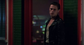 Movie still from “The Loveless” (1981), directed by Kathryn Bigelow – A man in a leather jacket standing next to a window; Medium shot, Low angle