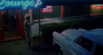 Movie still from “The Loveless” (1981), directed by Kathryn Bigelow – A woman standing in front of a white car; Wide shot, High angle