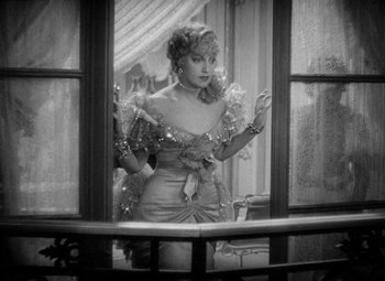 Movie still from “The Merry Widow” (1934), directed by Ernst Lubitsch – A black - and - white photo of a woman standing in front of an open window; Medium shot, Over the shoulder angle