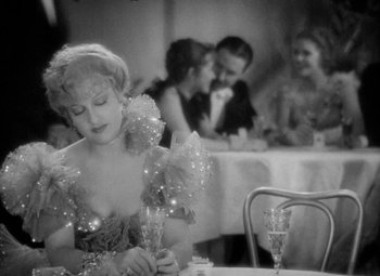 Movie still from “The Merry Widow” (1934), directed by Ernst Lubitsch – A woman sitting at a table with a glass of champagne; Medium shot, Over the shoulder angle