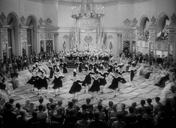 Movie still from “The Merry Widow” (1934), directed by Ernst Lubitsch – A group of people in a room with a large crowd; Extreme Wide shot, High angle
