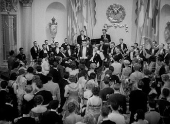Movie still from “The Merry Widow” (1934), directed by Ernst Lubitsch – An old photo of a group of people sitting in a room; Extreme Wide shot, High angle