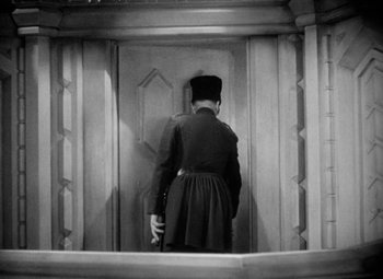 Movie still from “The Merry Widow” (1934), directed by Ernst Lubitsch – A man standing in front of an open door; Medium shot, Low angle