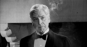Movie still from “The Mirror Crack'd” (1980), directed by Guy Hamilton – An older man in a tuxedo smoking a cigarette; Close Up shot, Low angle