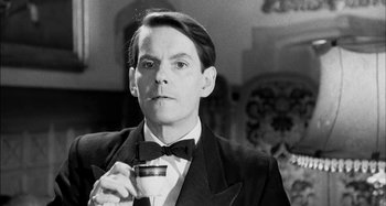 Movie still from “The Mirror Crack'd” (1980), directed by Guy Hamilton – A black and white photo of a man holding a glass of wine; Close Up shot, Low angle