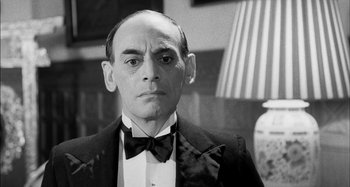 Movie still from “The Mirror Crack'd” (1980), directed by Guy Hamilton – A man wearing a suit and a bow tie; Close Up shot, Low angle