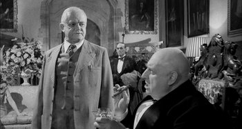 Movie still from “The Mirror Crack'd” (1980), directed by Guy Hamilton – Two men smoking and drinking in front of a painting; Medium shot, Low angle