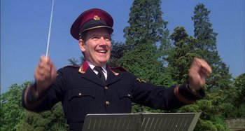 Movie still from “The Mirror Crack'd” (1980), directed by Guy Hamilton – A man in a military uniform is smiling; Medium shot, Low angle