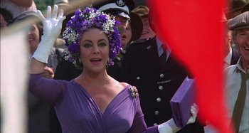 Movie still from “The Mirror Crack'd” (1980), directed by Guy Hamilton – A woman in a purple dress with flowers in her hair; Close Up shot, Over the shoulder angle
