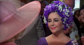 Movie still from “The Mirror Crack'd” (1980), directed by Guy Hamilton – A person wearing a hat with purple flowers on it; Close Up shot, Over the shoulder angle