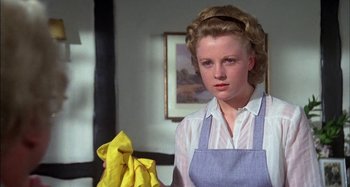 Movie still from “The Mirror Crack'd” (1980), directed by Guy Hamilton – A woman holding a yellow cloth in a room; Close Up shot, Low angle