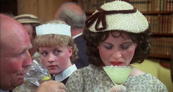 Movie still from “The Mirror Crack'd” (1980), directed by Guy Hamilton – A woman wearing a hat is holding a drink; Close Up shot, Over the shoulder angle