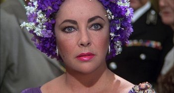 Movie still from “The Mirror Crack'd” (1980), directed by Guy Hamilton – A person wearing a purple flower crown; Close Up shot, Over the shoulder angle