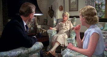 Movie still from “The Mirror Crack'd” (1980), directed by Guy Hamilton – An older woman sitting in a chair with two other people; Medium shot, Over the shoulder angle