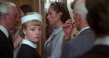 Movie still from “The Mirror Crack'd” (1980), directed by Guy Hamilton – A woman wearing a white hat is holding a glass of wine; Close Up shot, Over the shoulder angle