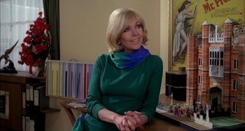 Movie still from “The Mirror Crack'd” (1980), directed by Guy Hamilton – A woman sitting at a desk in a green dress; Medium shot, Low angle