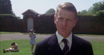 Movie still from “The Mirror Crack'd” (1980), directed by Guy Hamilton – A man wearing a suit and tie standing in front of a building; Close Up shot, Low angle