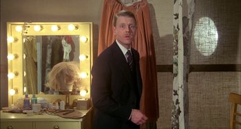 Movie still from “The Mirror Crack'd” (1980), directed by Guy Hamilton – A man standing in front of a mirror in a room; Medium shot, Over the shoulder angle