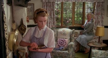 Movie still from “The Mirror Crack'd” (1980), directed by Guy Hamilton – A woman in an apron is holding something in her hand; Medium shot, High angle