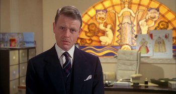 Movie still from “The Mirror Crack'd” (1980), directed by Guy Hamilton – A man wearing a suit and tie in front of a stained glass window; Close Up shot, Low angle
