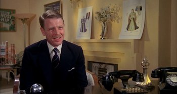 Movie still from “The Mirror Crack'd” (1980), directed by Guy Hamilton – A man sitting at a table in front of a microphone; Medium shot, Low angle