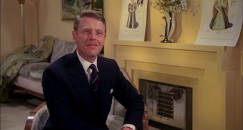 Movie still from “The Mirror Crack'd” (1980), directed by Guy Hamilton – A man sitting in front of a fireplace in a room; Medium shot, Low angle