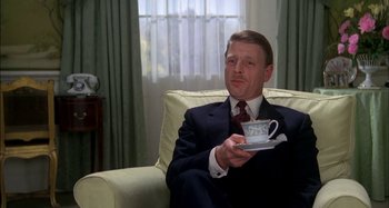 Movie still from “The Mirror Crack'd” (1980), directed by Guy Hamilton – A man sitting in a chair holding a cup of coffee; Medium shot, Low angle
