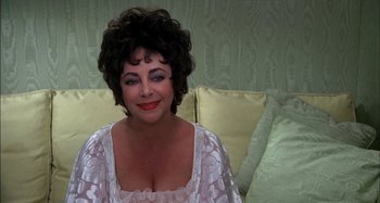 Movie still from “The Mirror Crack'd” (1980), directed by Guy Hamilton – A person sitting on a couch wearing a dress; Close Up shot, High angle