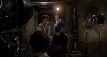 Movie still from “The Mirror Crack'd” (1980), directed by Guy Hamilton – A woman in a purple dress standing next to a man in a yellow shirt; Wide shot, Over the shoulder angle