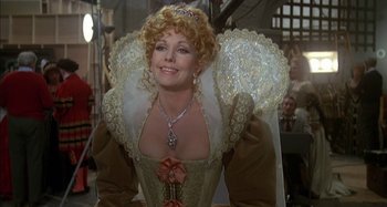 Movie still from “The Mirror Crack'd” (1980), directed by Guy Hamilton – A woman in a medieval dress smiling for the camera; Close Up shot, Over the shoulder angle