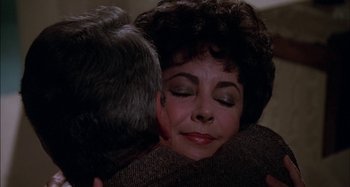 Movie still from “The Mirror Crack'd” (1980), directed by Guy Hamilton – An older man hugging a beautiful woman in a dark room; Close Up shot, Over the shoulder angle