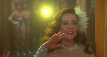 Movie still from “The Mirror Crack'd” (1980), directed by Guy Hamilton – An older woman in a silver dress and a white flower in her hair; Close Up shot, Over the shoulder angle