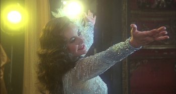 Movie still from “The Mirror Crack'd” (1980), directed by Guy Hamilton – A woman in a white dress is holding her arms up; Close Up shot, Over the shoulder angle