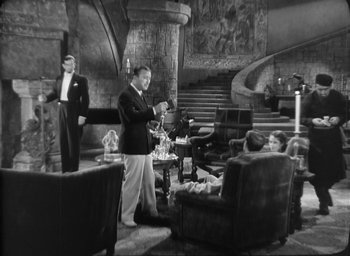 Movie still from “The Most Dangerous Game” (1932), directed by Irving Pichel – A man standing in a living room next to two other men; Wide shot, High angle