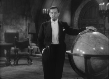 Movie still from “The Most Dangerous Game” (1932), directed by Irving Pichel – A man in a suit standing in front of a globe; Medium shot, High angle