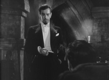 Movie still from “The Most Dangerous Game” (1932), directed by Irving Pichel – A black and white photo of a man in a tuxedo holding a cell phone; Medium shot, Over the shoulder angle
