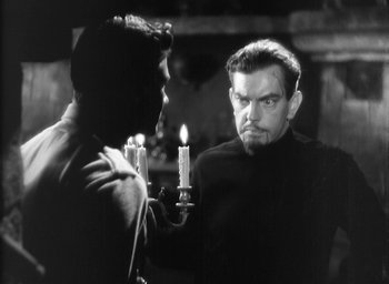 Movie still from “The Most Dangerous Game” (1932), directed by Irving Pichel – A man holding a candle in front of another man; Medium shot, Over the shoulder angle