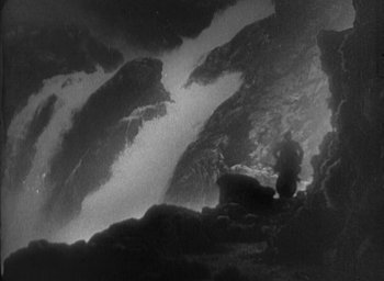 Movie still from “The Most Dangerous Game” (1932), directed by Irving Pichel – A black - and - white photo of a person standing in front of a waterfall; Extreme Wide shot, High angle
